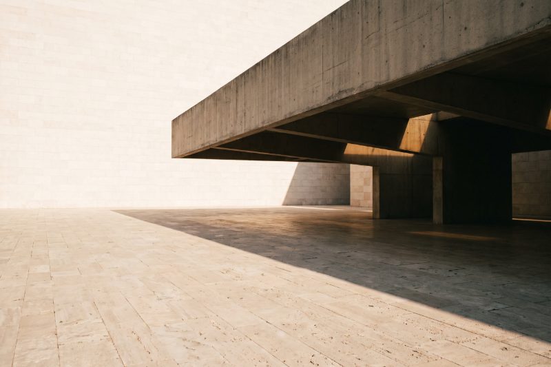 A wide concrete canopy casting a geometric shadow over a limestone plaza in morning light
